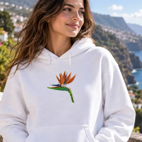 White hoodie embroidered with a bird of paradise flower, Madeira's coast behind